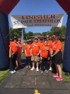 MNDBC members standing under the finish line banner for the St. Paul Triathlon after volunteering for the morning with the event.