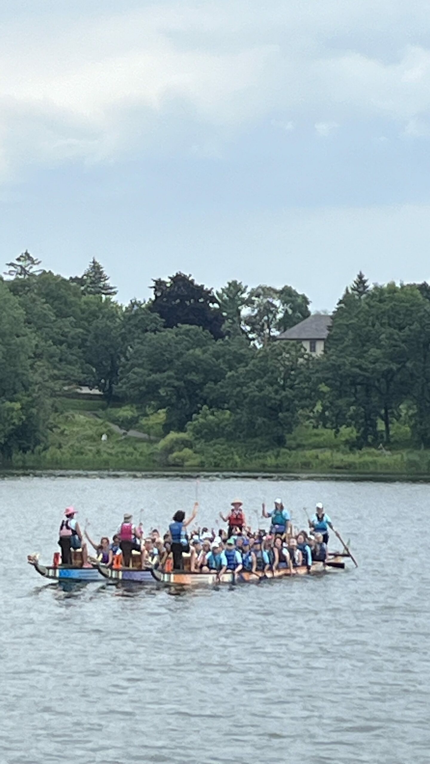 Three dragon boats are "rafted" together on the lake as paddlers hold pink carnations high in the air during the Cancer Survivors ceremony